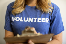 A woman with a clipboard wearing a blue t-shirt saying, "volunteer."