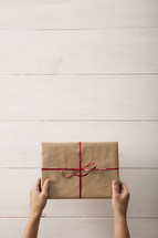 Placing a gift wrapped in brown paper and red ribbon on a white washed wooden table.