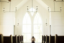 Woman praying in front of a window in a church.