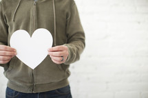 A man stands holding a white paper heart.