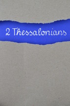 2 Thessalonians - torn open kraft paper over intense blue paper with the name of the second letter from Paul to the Thessalonians