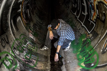 Man spray painting graffiti in a sewerdrain pipe.