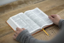 A person reading the Bible on a wooden table.