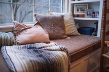 a window bench seat with throw pillows and a blanket 