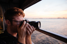 a man with a camera taking a picture from a ferry at sunset 