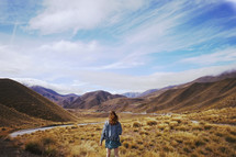 a woman standing in grass in a valley surrounded by mountains 