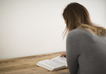A woman reading the Bible at a wooden table.