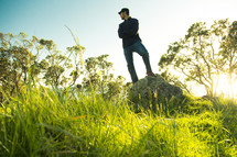 man standing outdoors with his foot on a rock looking behind 
