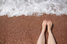 Travel concept - Woman's legs on beautiful tropical beach with pebble sand. Feet on sand and wave in summer time. girl barefoot in ocean water on vacation travel. Feel happy and relax. copy space