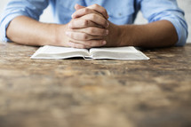 man's hands in prayer on an open Bible 