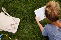 a woman lying in the grass reading a Bible.