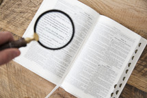 hand holding a magnifying glass over a Bible 