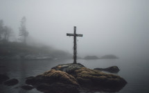 Wooden cross on a small island shrouded in fog.