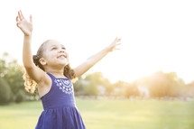 Happy, young girl standing outdoors with raised arms in praise. 