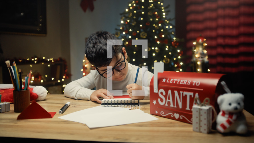 Kid writing Christmas letter on his notebook 