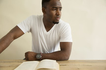 an African American man thinking while reading a book.