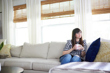 a woman sitting on the couch holding a coffee mug 