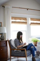 a woman sitting in an arm chair reading a Bible 