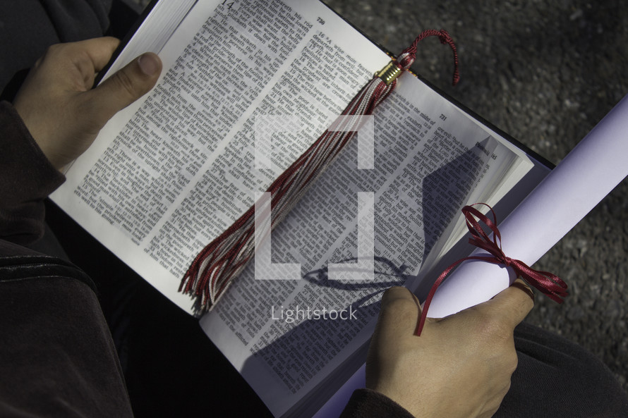 student reading a Bible holding a diploma and graduation tassel