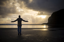 a man standing on a beach with outstretched arms 