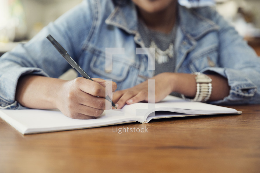 an African American woman sitting at a table writing in a journal  