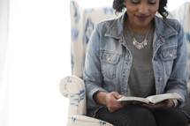 an African American woman sitting in a chair reading a Bible 