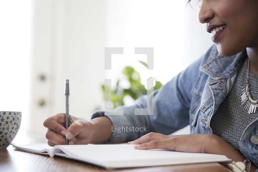 an African American woman sitting at a table writing in a journal 