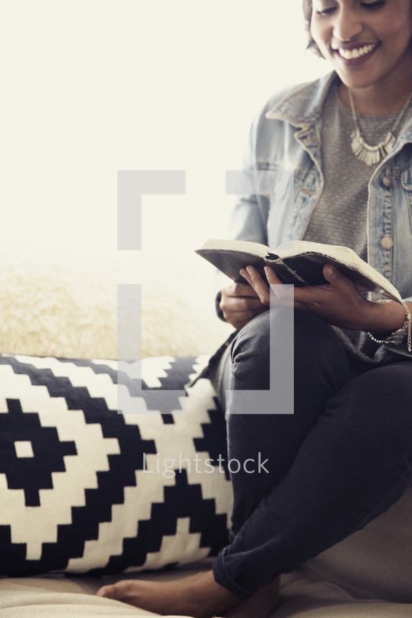 An African American woman sitting in a chair reading a Bible 
