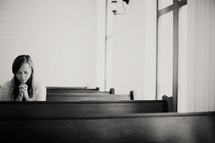 Woman praying in a church pew.