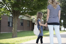 A mother and daughter holding hands outside of an elementary school.