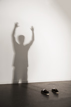 shadow of a man with raised arms and shoes on the floor 