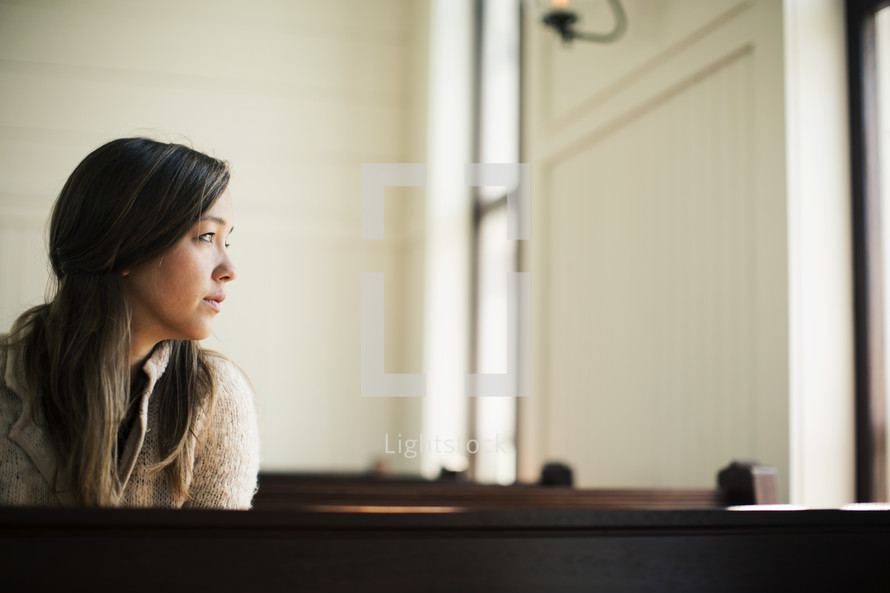 Woman looking out the window while sitting in a church pew.