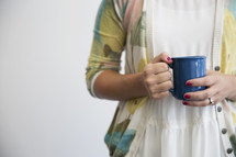 A woman in a sweater holding a blue coffee cup.