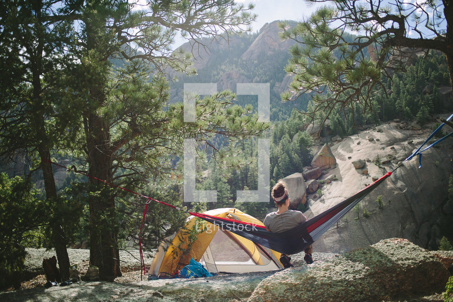 a woman in a hammock next to a tent in a campsite 