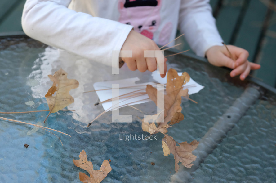 kid playing with leaves and pine straw on a glass table 