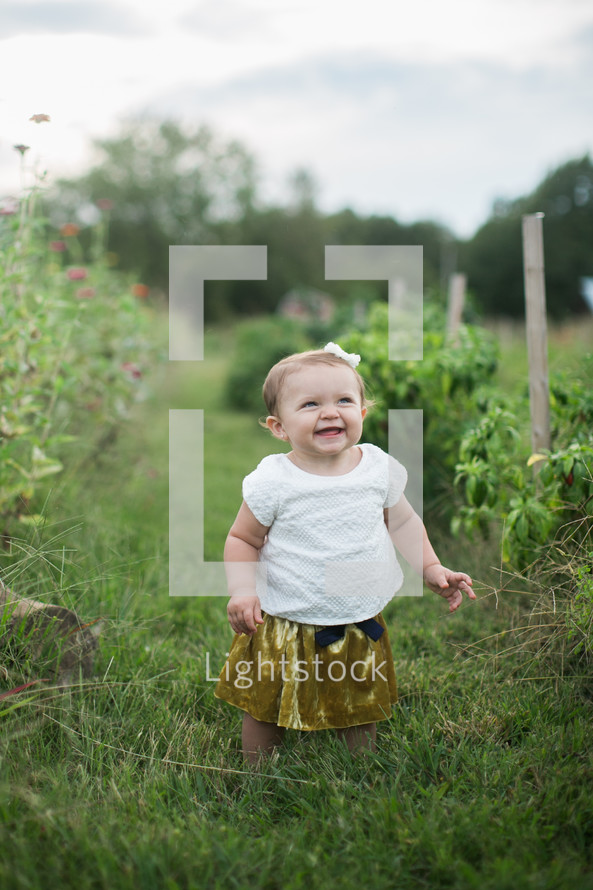 a smiling toddler girl standing in grass 