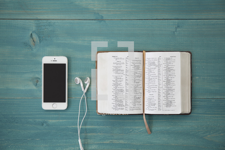 iphone 6 and earbuds and open Bible on a teal table 