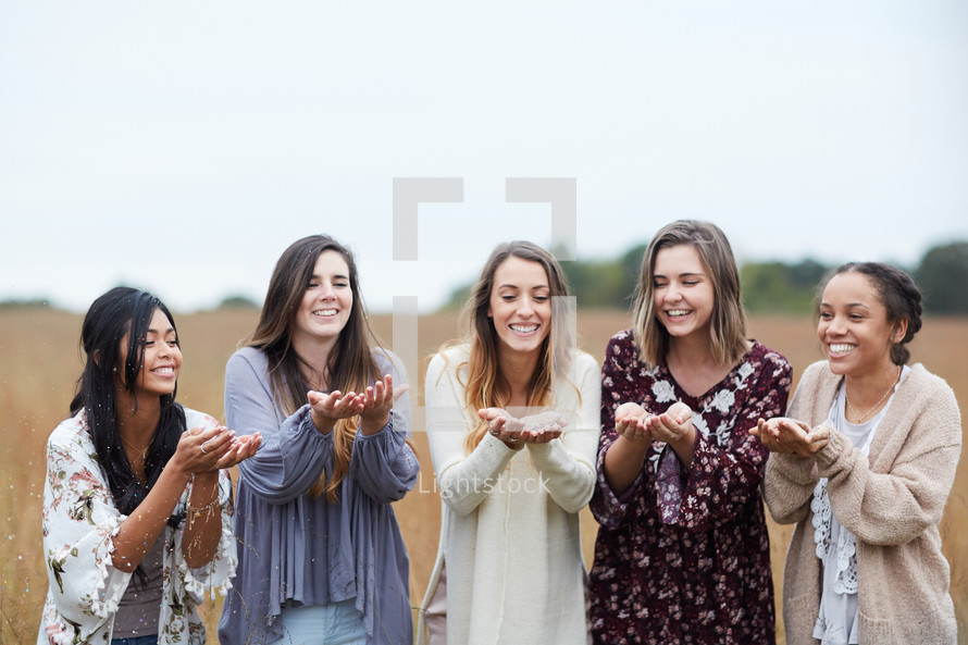 group of young women blowing confetti standing in a field 