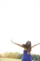 Girl standing outside with arms raised.