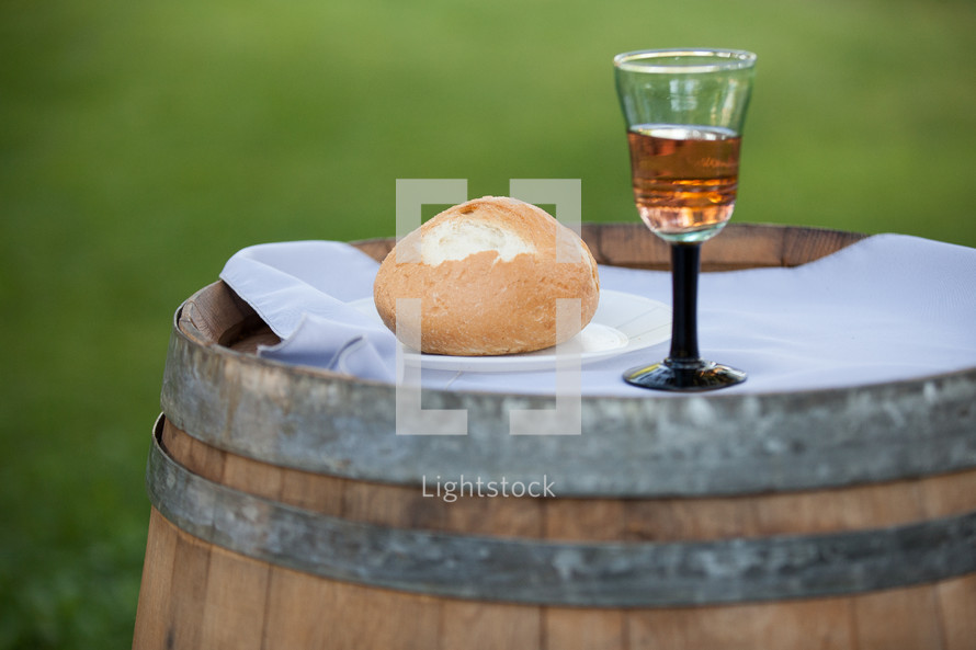 A glass of wine and a bread roll, sitting on a wine barrel