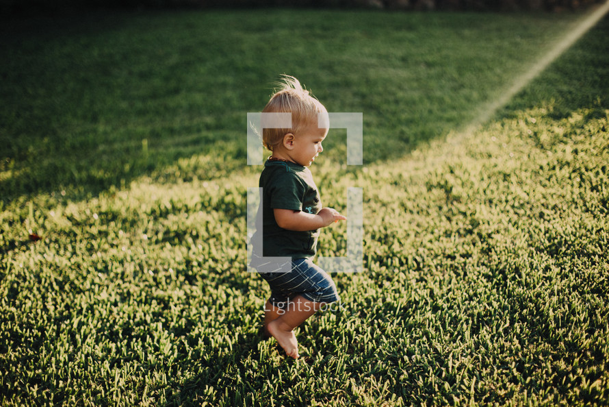 a toddler boy running through a sprinkler in the grass 