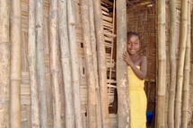 A young African girl peeking out of a bamboo hut 