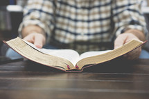 a man in a plaid shirt reading a Bible on a coffee table 