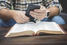 a man texting on his cellphone over the pages of an open Bible 