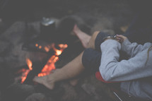 woman holding a mug sitting by a campfire 