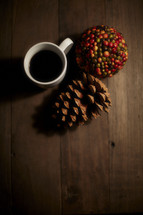 coffee cup, pine cone, and berries on a wood table