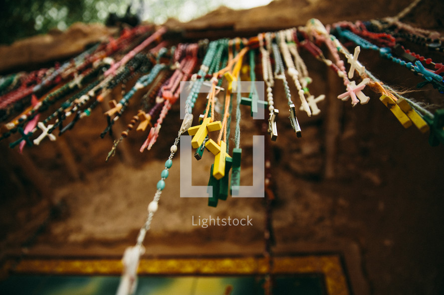 Multi-colored rosary beads hanging on a rod outdoors.
