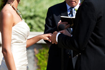 Groom placing ring on bride's hand during outdoor wedding ceremony.