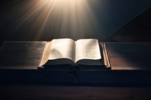 Open holy bible on wooden table with rays of light in dark room