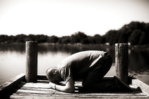 Man kneeling in prayer on river dock